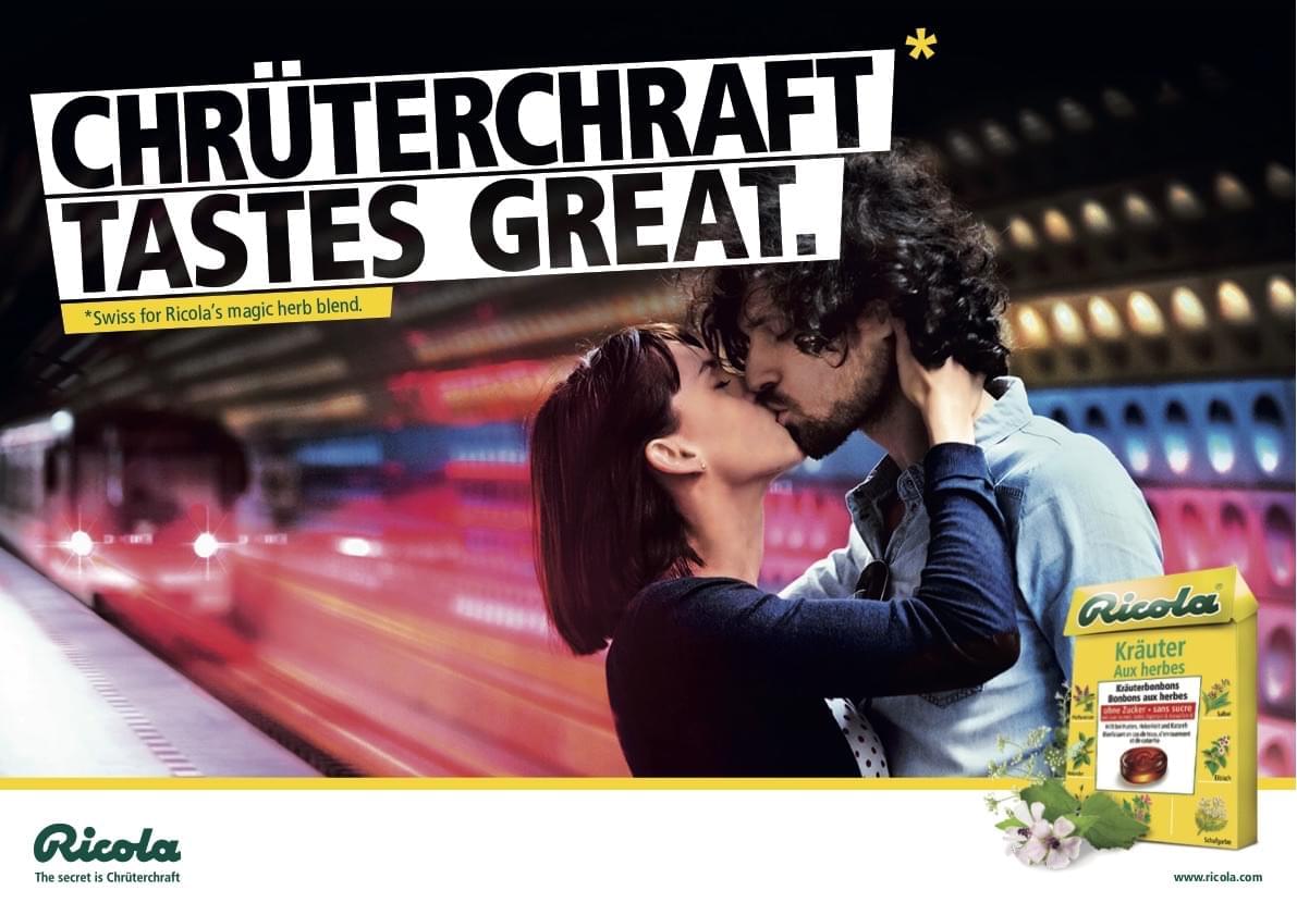The ad shows a kissing couple in a subway train station. The headline says 'Chrüterchraft tastes great. Swiss for ricolas magic herb blend.'